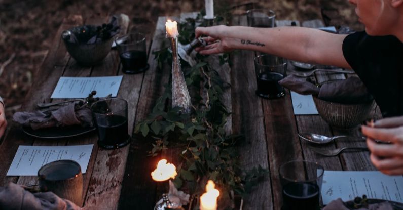 California Wine Eco - From above of crop young female at timber table with glasses of wine and decorated with candles and green leaves